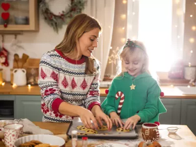 A mother and daughter baking holiday cookies together in a decorated kitchen