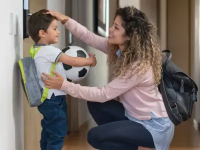 A mum saying goodbye to her son before the childcare or school drop-off,  giving him a pat on the head while he holds a football