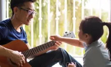 Dad plays guitar as child points to frets