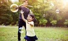 happy little girl blowing bubbles with parent in background