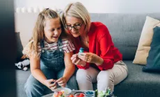 A grandmother and her granddaughter sitting on the couch, enjoying arts and crafts together at a table.