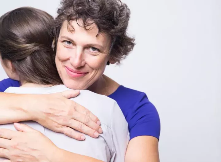 mother embracing teenage girl while looking at camera