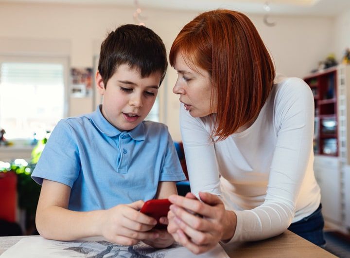 Smiling boy using smartphone with his mother at home