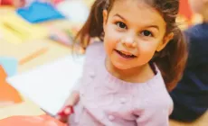 little girl using scissors smiles up at camera