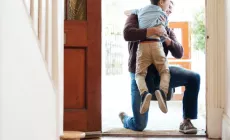 A young boy runs into his father’s arms at the front door.